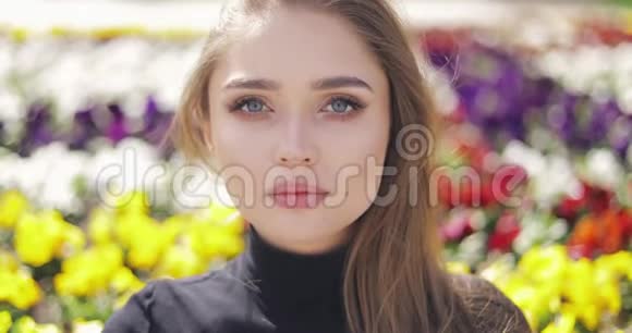 美丽的女性蓝色的眼睛和化妆在模糊的彩色花朵背景上视频的预览图