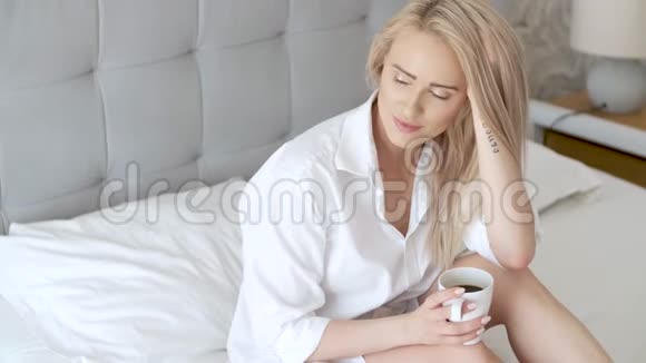 美丽的金发女人在家坐在床上喝咖啡视频的预览图