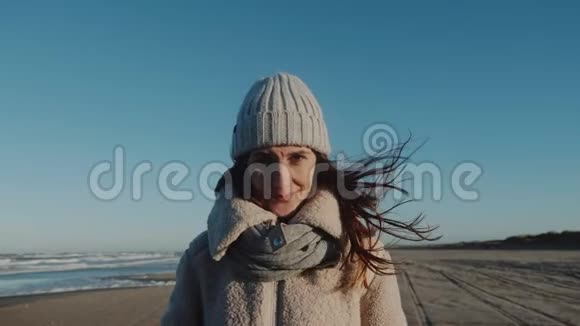 美丽微笑的白人旅游妇女的肖像看着镜头在惊人的风冬海岸慢动作视频的预览图