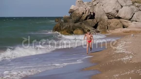 男孩沿着海岸线跑海浪在海滩上冲刷那个男孩沿着海滩跑戴眼镜的那个孩子视频的预览图