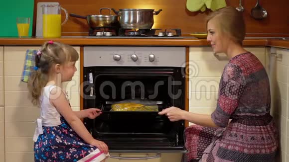年轻的妈妈在厨房教可爱的女儿做饭幸福的家庭小女孩帮妈妈做饭美味的食物视频的预览图
