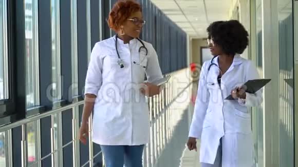 在医院里忙碌的非裔美国医生一边说话一边穿过大楼全新的现代功能视频的预览图