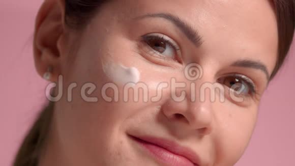 30岁的黑发女人的特写肖像脸颊上抹着奶油做一些面部按摩视频的预览图