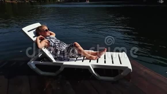 小女孩躺在太阳床上戴着太阳镜和一条薄纱披肩儿童在洪水木水下码头休息人行道视频的预览图