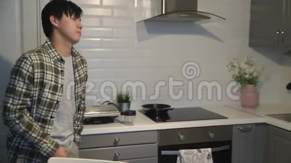 沉睡的亚洲男人倒咖啡在杯子里在家里的厨房里拿饼干视频的预览图