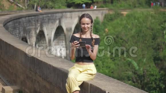 女孩在丛林中坐在老桥墙上自拍视频的预览图