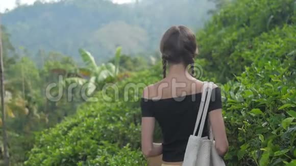 年轻女子带着包走在小路上闻着茶叶的味道视频的预览图