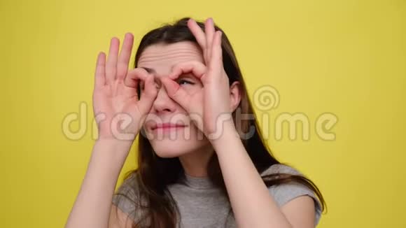 有趣的年轻女人玩着用手做眼镜的形状在工作室里睁大眼睛做滑稽的脸视频的预览图