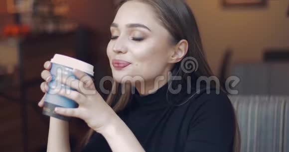 年轻漂亮的女孩蓝眼睛坐在咖啡屋里喝着咖啡视频的预览图