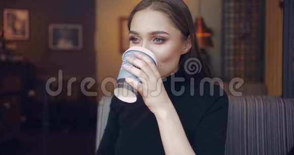 温柔的年轻女子小心翼翼地拿着一杯咖啡喝着视频的预览图