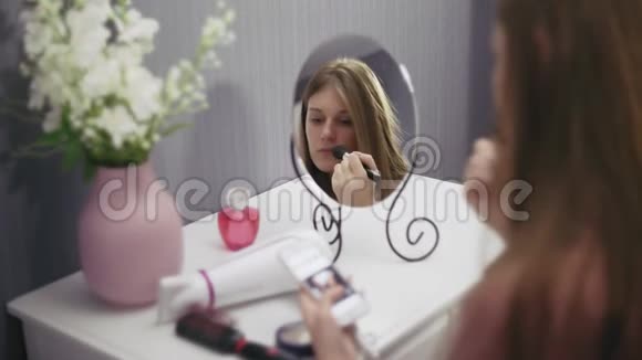 年轻漂亮的女人拿着刷子涂红粉用智能手机视频的预览图