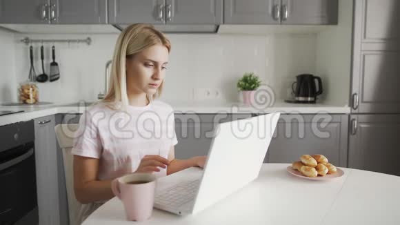 自由职业者喝咖啡在厨房用笔记本电脑做笔记本的女商人视频的预览图