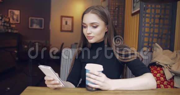 穿着休闲服装端着咖啡用智能手机的年轻美女视频的预览图