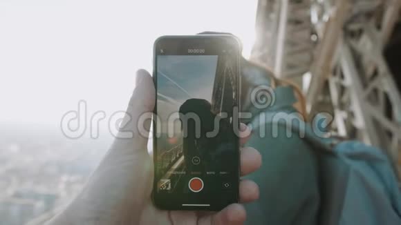 一只雄性手正在拍摄一段智能手机视频视频中快乐的微笑着的女人在埃菲尔铁塔顶上摆姿势浪漫概念慢动作视频的预览图