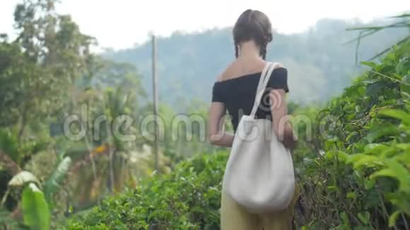 年轻女子带着包走在小路上闻着茶叶的味道视频的预览图