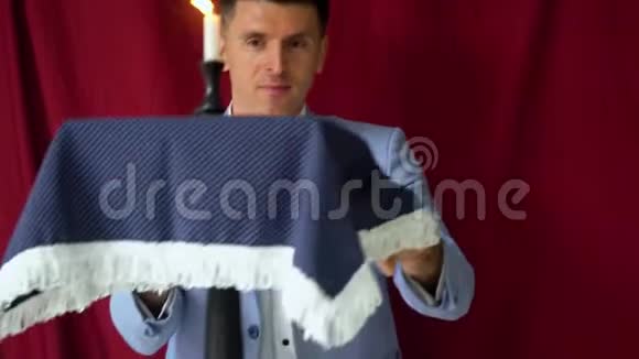 穿着西装的魔术师用桌子和蜡烛在昏暗的背景下表演魔术视频的预览图