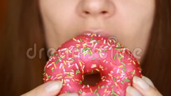特写女人吃一个粉红色的甜甜圈好吃甜甜饮食节食女人的嘴咬着甜点视频的预览图