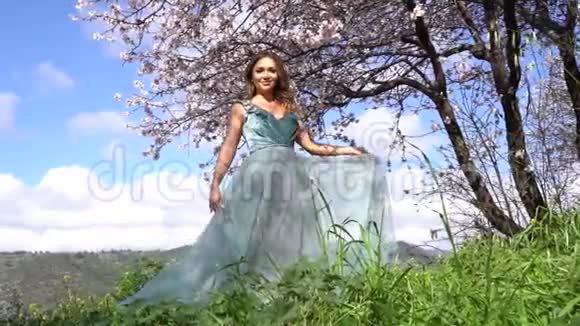 模特穿着华丽的服装摆着一棵盛开的杏树背景是一个山谷视频的预览图