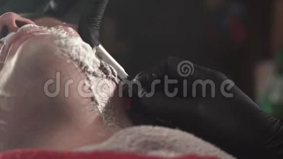 理发师戴黑色手套用直剃刀剪客户胡须特别刮胡霜适用于男士视频的预览图