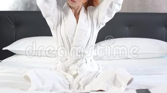 红发女孩穿着白色浴袍躺在酒店房间的床上视频的预览图