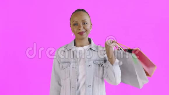 美国黑人妇女的肖像带购物袋和金钱风扇的粉红色背景在工作室牛仔裤夹克视频的预览图