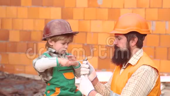 父亲和小儿子在车间用钻穿木板一对父子可爱的男孩在建房子父亲和视频的预览图