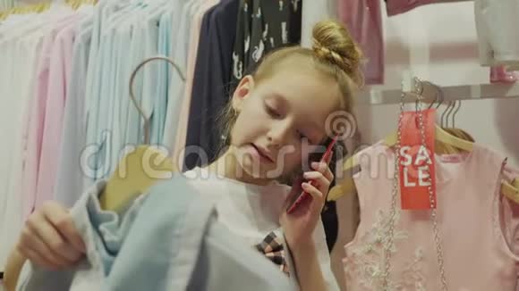 可爱的小女孩一边选择衣服一边打电话视频的预览图
