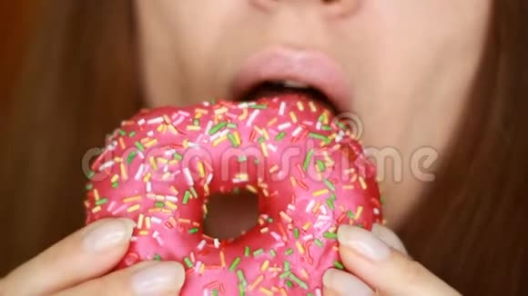 特写女人吃一个粉红色的甜甜圈好吃甜甜饮食节食女人的嘴咬着甜点视频的预览图