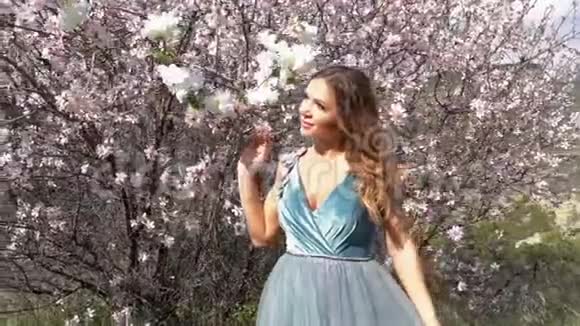 模特穿着华丽的服装摆着一棵盛开的杏树背景是一个山谷视频的预览图