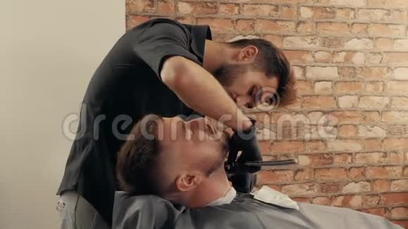 理发店里用直剃刀给留胡子的人刮脖子理发师用直剃须刀刮胡子视频的预览图
