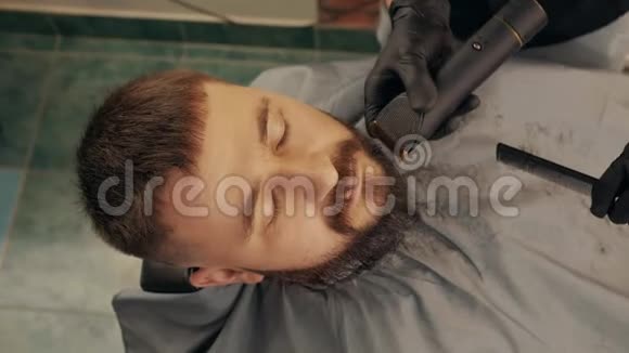 在理发店用电动剃须刀刮胡子的胡子俯视图中英俊的男子修剪胡须视频的预览图