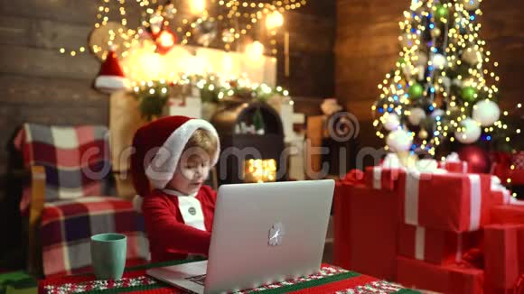 可爱的孩子带着笔记本电脑在家里的圣诞节背景圣诞快乐孩子新年快乐圣诞礼物视频的预览图