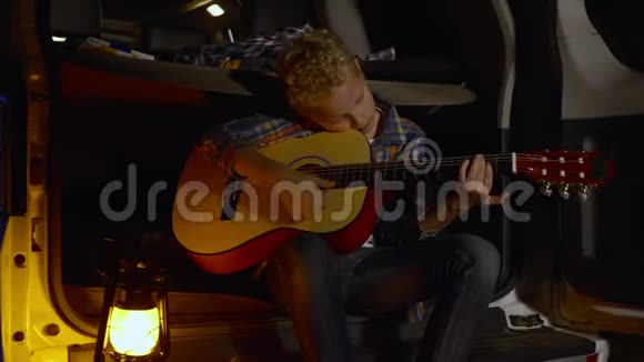 小男孩吉他手在森林徒步旅行中在汽车后备箱上弹吉他带游客玩吉他音乐的少年男孩视频的预览图