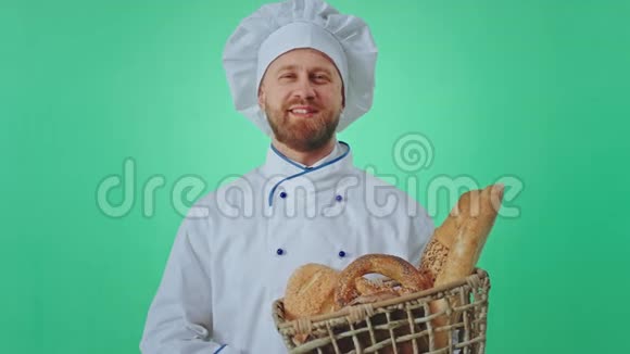 有魅力的金发面包师男人拿着一个装满新鲜面包的篮子在一个绿色的工作室里他笑得大大的视频的预览图