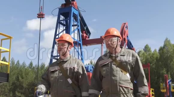 两名石油工人监督原油生产钻机工业油井泵千斤顶用于抽取原油视频的预览图