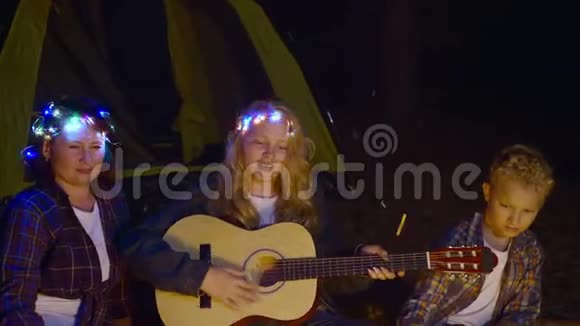 欢快的女孩弹吉他一起唱着歌妈妈和哥哥在夜林的篝火前女孩视频的预览图