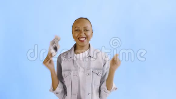 满意高兴兴奋非洲裔美国妇女展示钱和说YEAH在蓝色背景让夹克视频的预览图