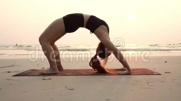 亚洲年轻女子练习瑜伽桥日落时在沙滩上摆姿势视频的预览图