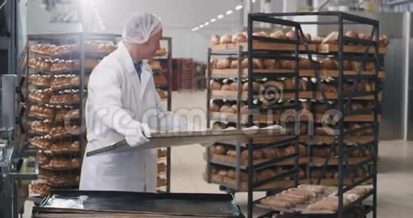 老面包师拿着生面包的托盘装到架子上把面团运到烤面包里视频的预览图