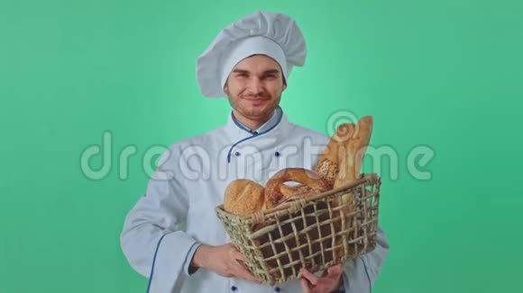 漂亮的面包师在镜头前的绿色工作室拿着一个篮子里面有新鲜的法国面包他很有魅力视频的预览图