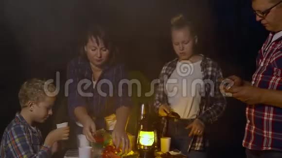 旅游家庭在晚上吃烧烤香肠和蔬菜夏天在黑暗中露营旅行家庭用餐视频的预览图