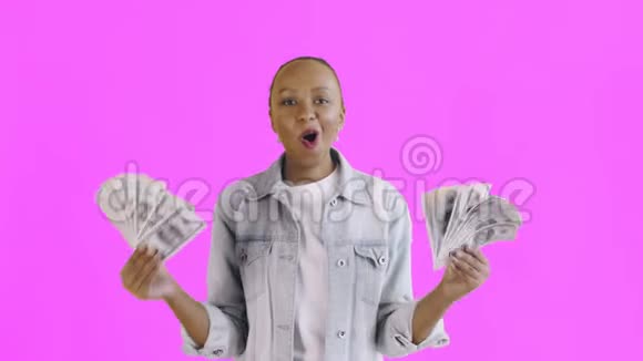 满意的兴奋的兴奋的非裔美国女人在粉红色的背景上展示金钱说上帝啊让夹克视频的预览图