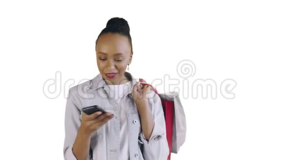 美国黑人妇女带着购物袋的肖像正在白色背景上通过智能手机录制语音信息视频的预览图
