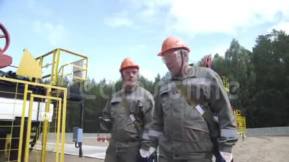 两名工人在油泵千斤顶附近走来走去监督原油生产现场的石油工程师视频的预览图