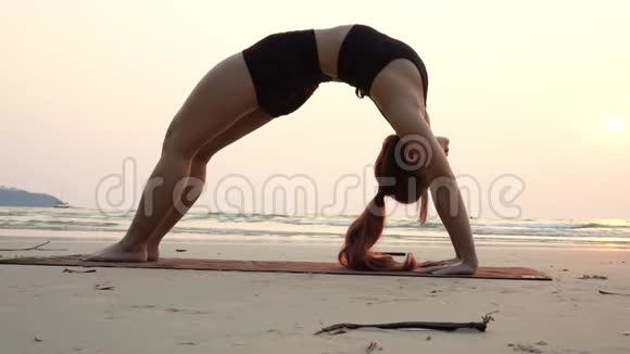 亚洲年轻女子在沙滩上练习瑜伽桥视频的预览图