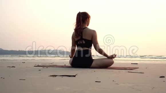 背面的观点女人练习瑜伽莲花姿势冥想与暑假在海滩上视频的预览图