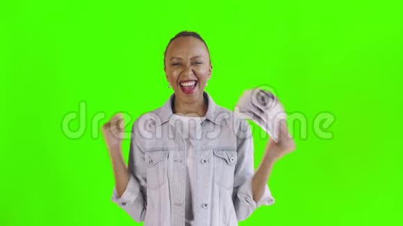 满意的兴奋的兴奋的非裔美国妇女在绿色背景的Jean夹克上展示金钱和相机跳舞视频的预览图