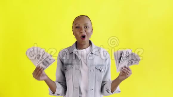 满意的兴奋的兴奋的非裔美国妇女在黄色背景的Jean夹克上展示金钱说上帝啊视频的预览图