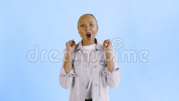 美丽快乐的非洲年轻女子说哦我的上帝在蓝色背景的Jean夹克上跳舞视频的预览图