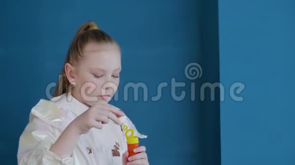 可爱的少年女孩在工作室的蓝色墙壁背景上吹肥皂泡有雀斑的女学生视频的预览图